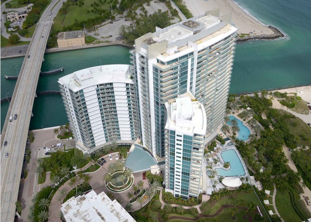 A curved high-rise complex with two exterior pools, all with a pristine white finish that contrasts the blue water nearby.