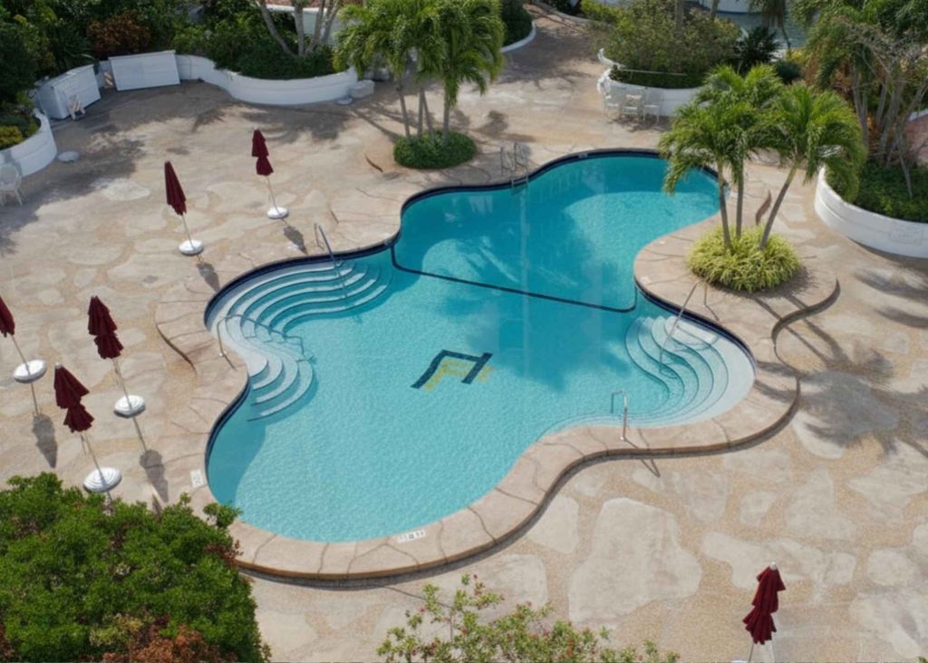 A lagoon-shaped pool with curved steps on each side and a beach-inspired pool deck with umbrellas.